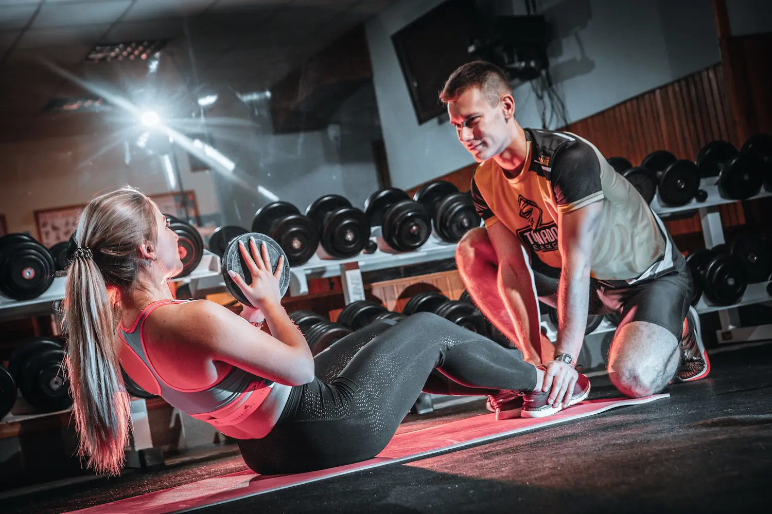 Coach accompagnant une pratiquante pendant un exercice abdominal avec une charge