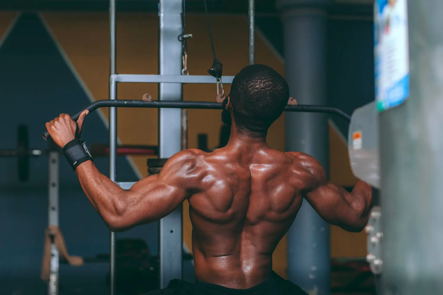 Pratiquant vu de dos réalisant un tirage à la poulie haute en salle de musculation